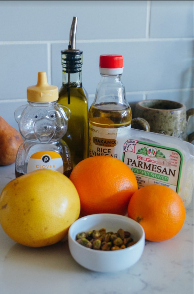 pistachio and honey citrus salad recipe ingredients: various citrus fruits, pistachios in bowl, parmesan cheese, honey, rice vinegar, and olive oil on counter top