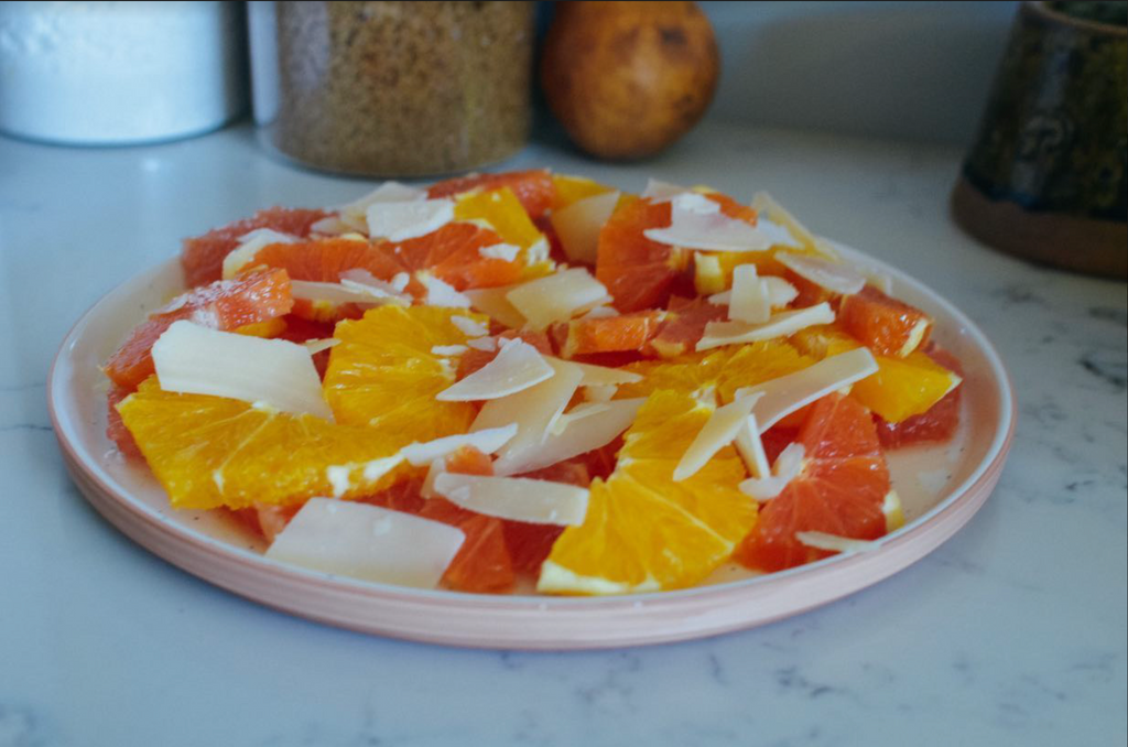 pistachio and honey citrus salad recipe: sliced citrus fruits with shaved parmesan on plate