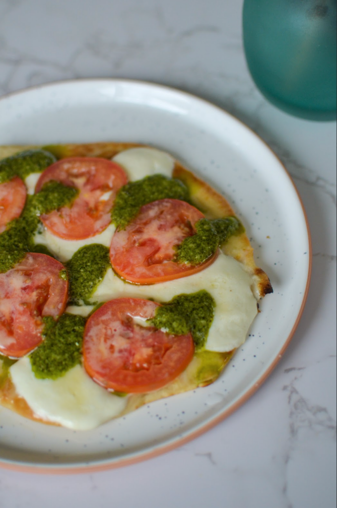 caprese flatbread on a plate with tomato, mozzarella, and pesto 